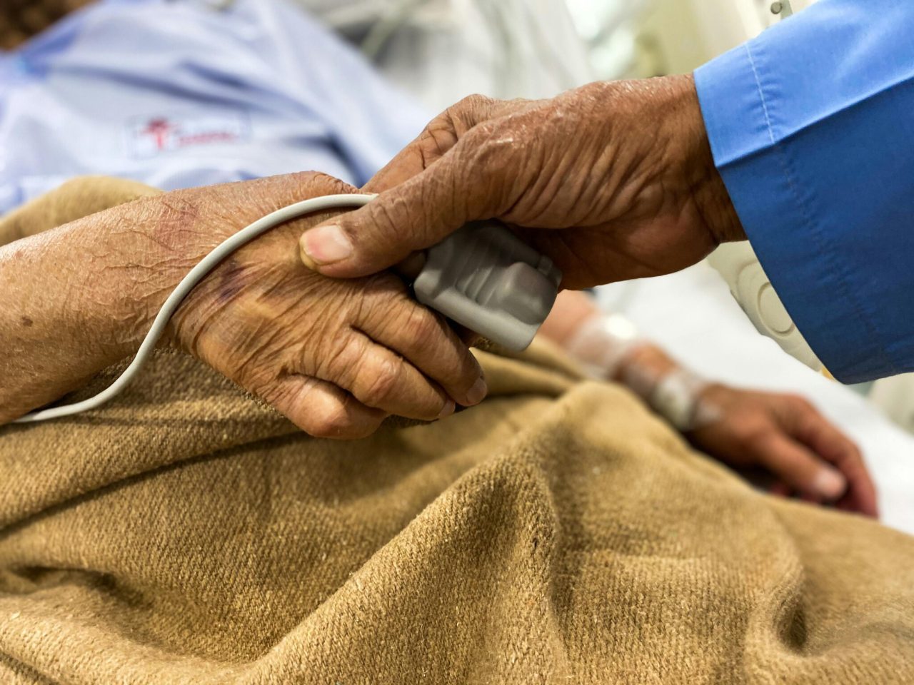 A carer holding the hand of a patient being monitored in hospital after collapsing