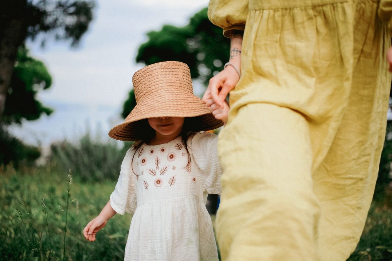 A young girl in a straw hat holding her mother's hand while walking through long grass