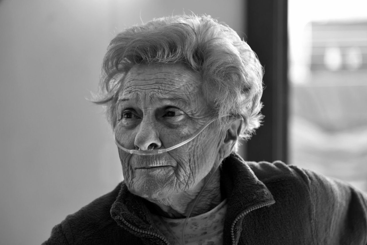 Black and white portrait of an older woman at home wearing a nasal oxygen cannula, looking to one side
