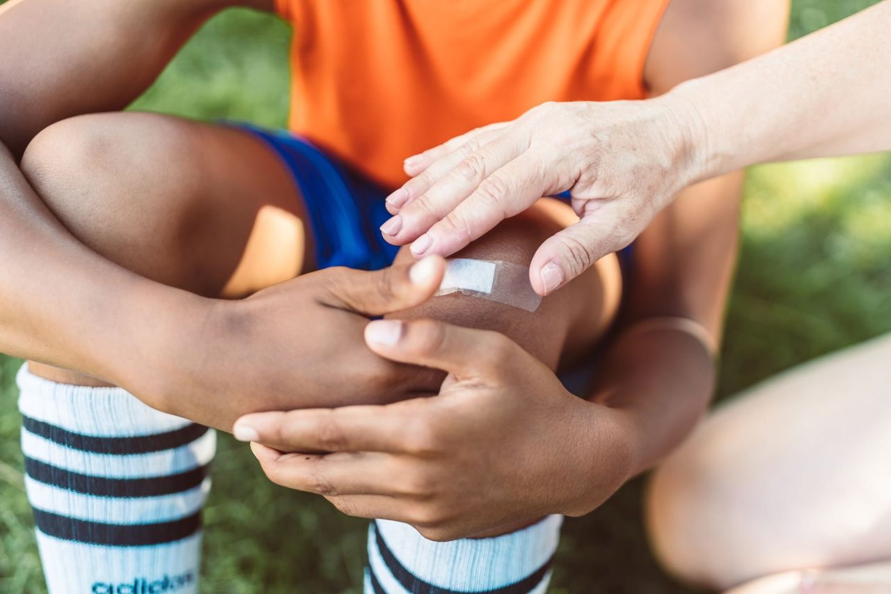 An adult pressing a plaster onto a child's knee on the grass after a fall during sport