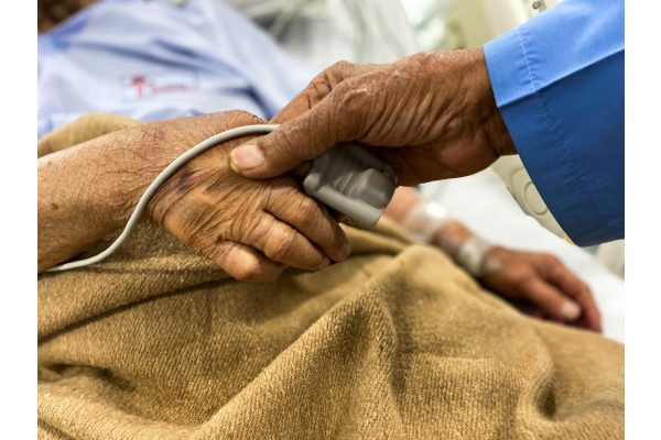 A carer holding the hand of a patient being monitored in hospital after collapsing