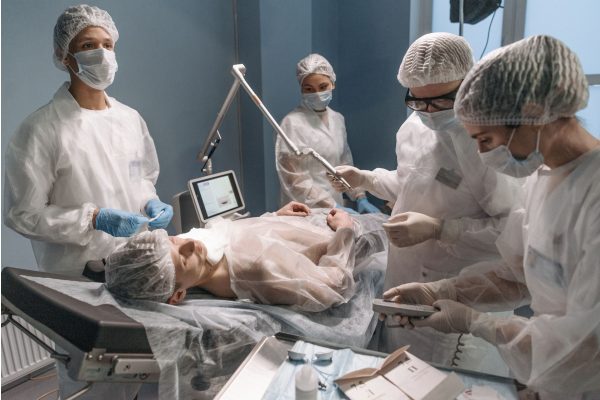 An operating theatre team in caps and gowns working around a patient under anaesthesia