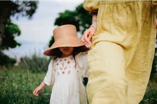 A young girl in a straw hat holding her mother's hand while walking through long grass