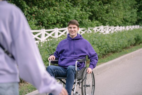 A smiling young man in a purple hoodie sitting in his wheelchair on a garden path