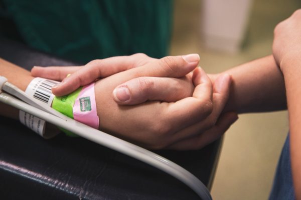 A patient's hand with an IV line and hospital wristband, held gently by another person's hands