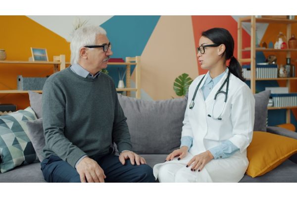 An older man in a grey jumper talking with a doctor in a white coat in a bright clinic room