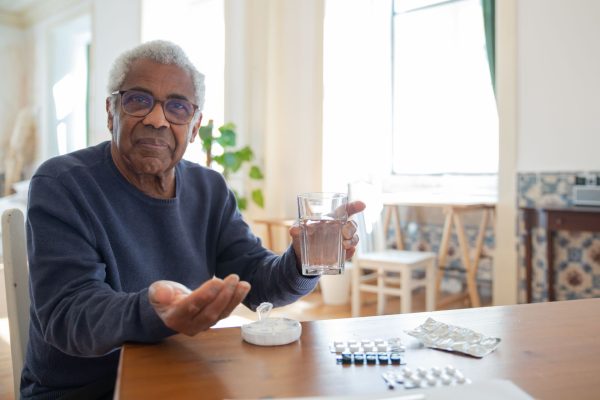 An older man sitting at his kitchen table with a glass of water and his morning tablets laid out in front of him