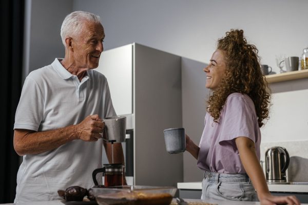 An older man and his adult granddaughter laughing together over coffee in a bright kitchen