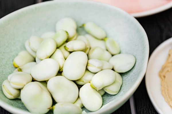 A pale green ceramic bowl filled with shelled fava beans on a dark wooden table